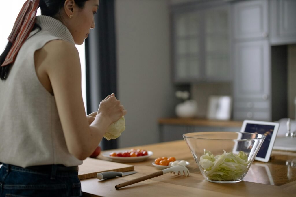 Asian woman preparing a fresh salad with tomatoes and lettuce in a contemporary kitchen setting.